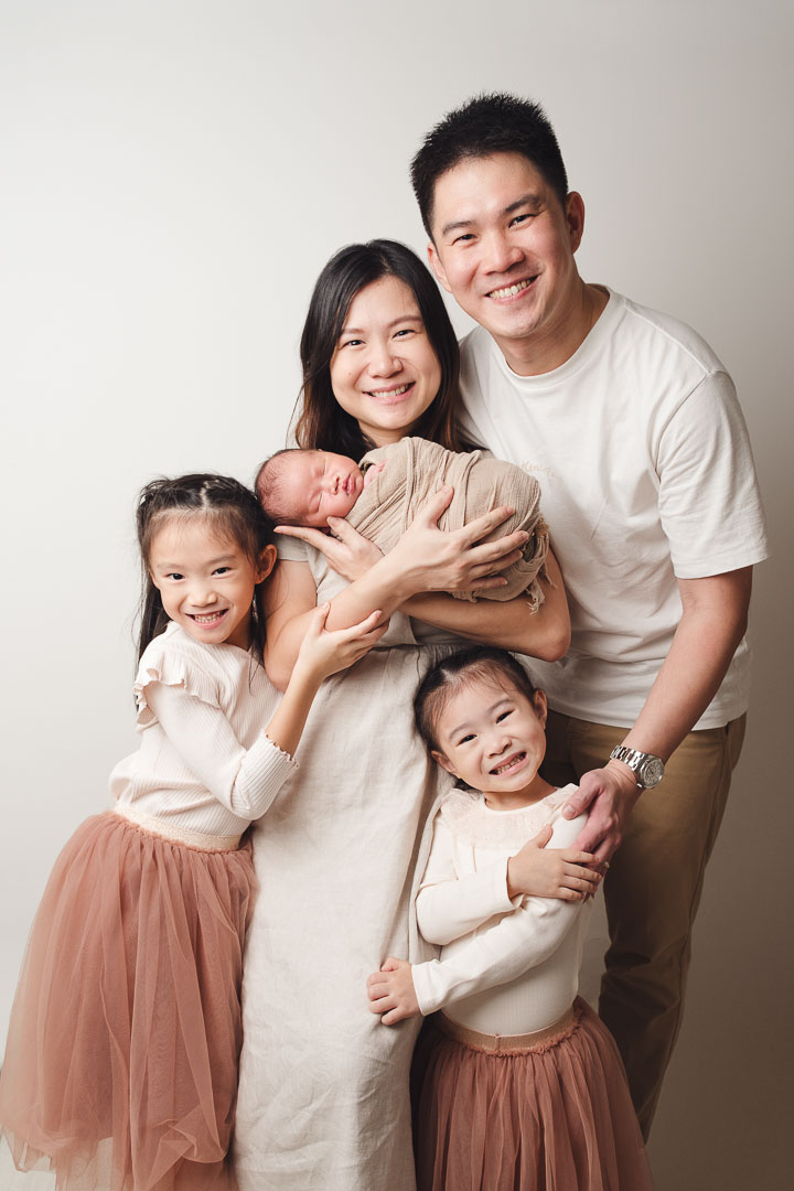 Family of 5 posing in neutral tone outfits with their newborn baby