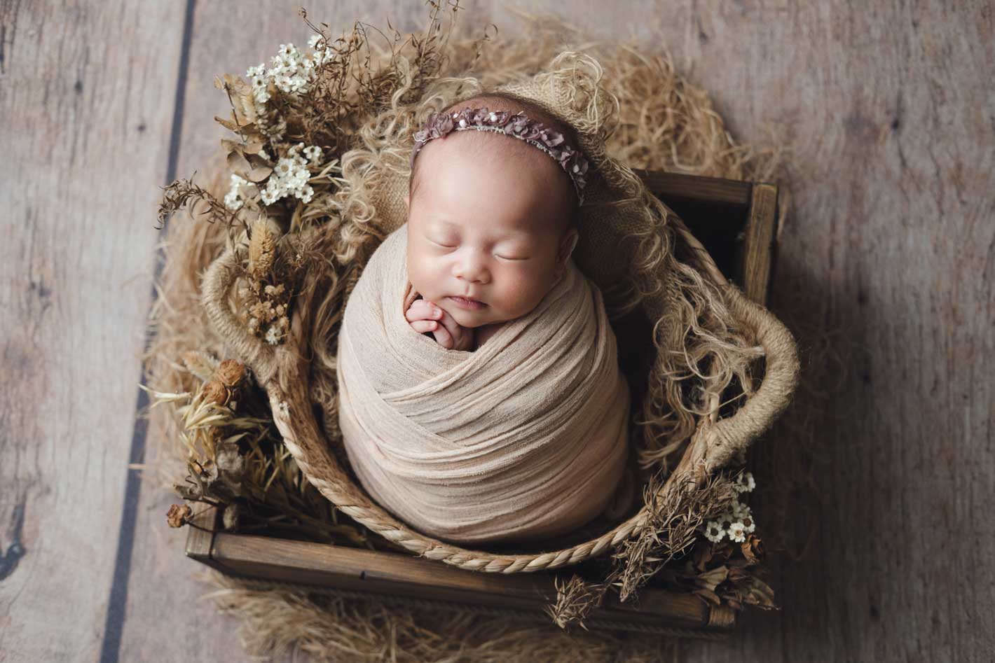 Newborn baby curled in a rustic wicker crate surrounded by delicate dried botanicals, Singapore