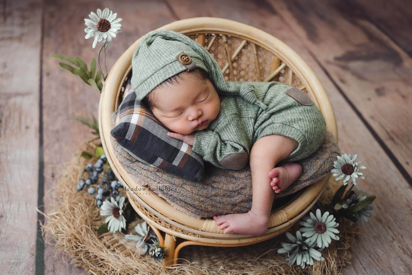 newborn baby in green vintage outfit posing on round rattan prop stool
