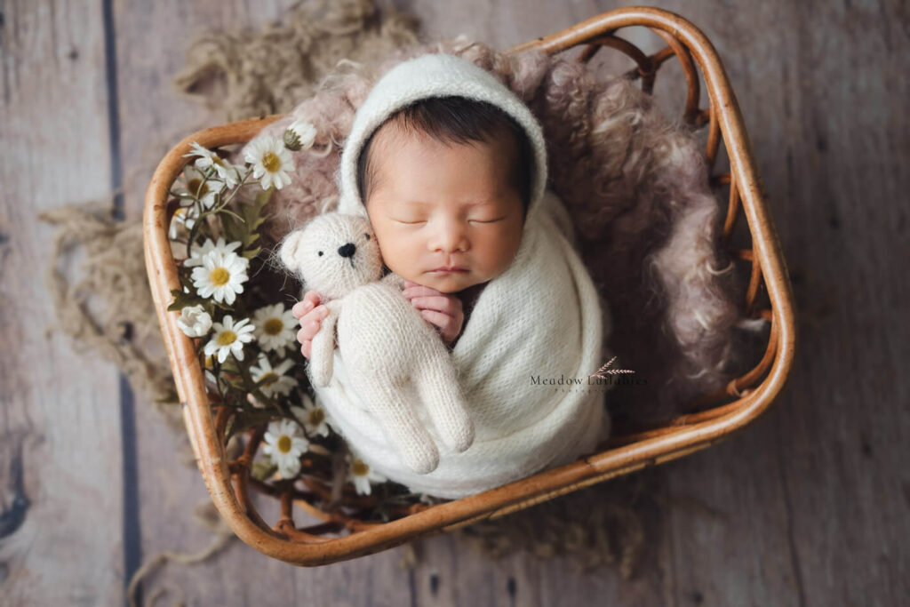 Gently wrapped newborn sleeping in a rattan basket adorned with white daisies, newborn photography Singapore