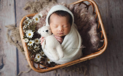 Gently wrapped newborn sleeping in a rattan basket adorned with white daisies, newborn photography Singapore