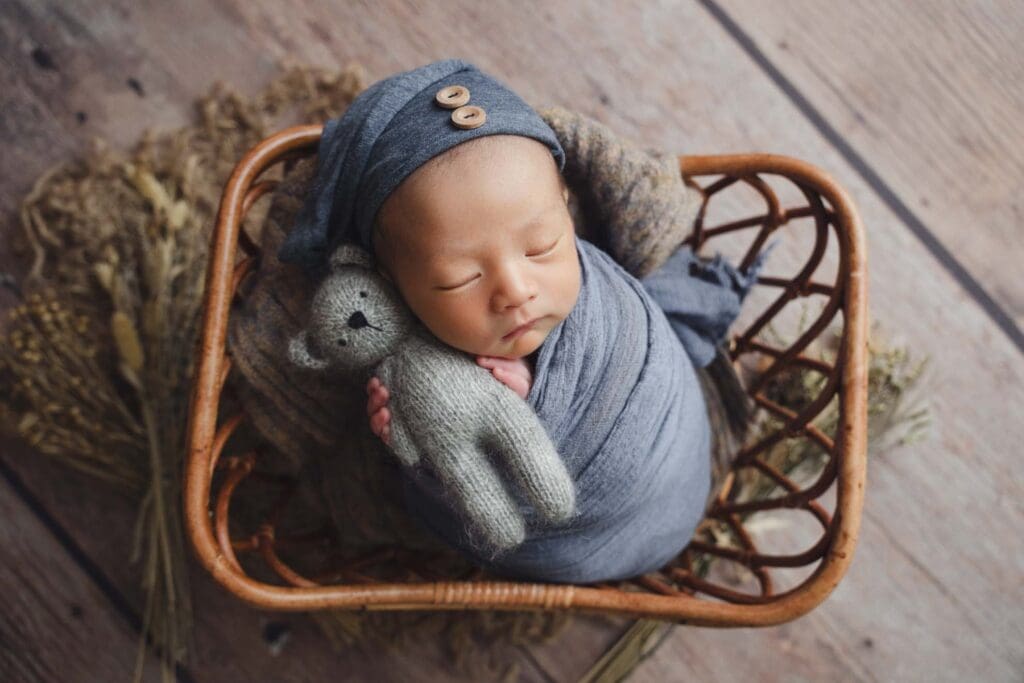 Newborn Photography Singapore Newborn photoshoot - Little newborn baby wrapped in blue in a wooden prop clutching his little blue bear soft toy