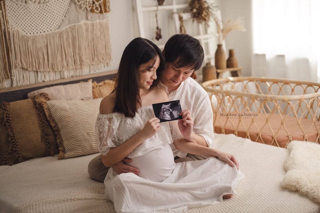Maternity Photography Singapore Couple in heartfelt moment posing on bed looking at their baby's ultrasound scan