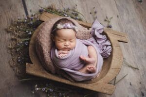 Newborn baby in wrapped in lavender wrap posing in wooden dough bowl prop
