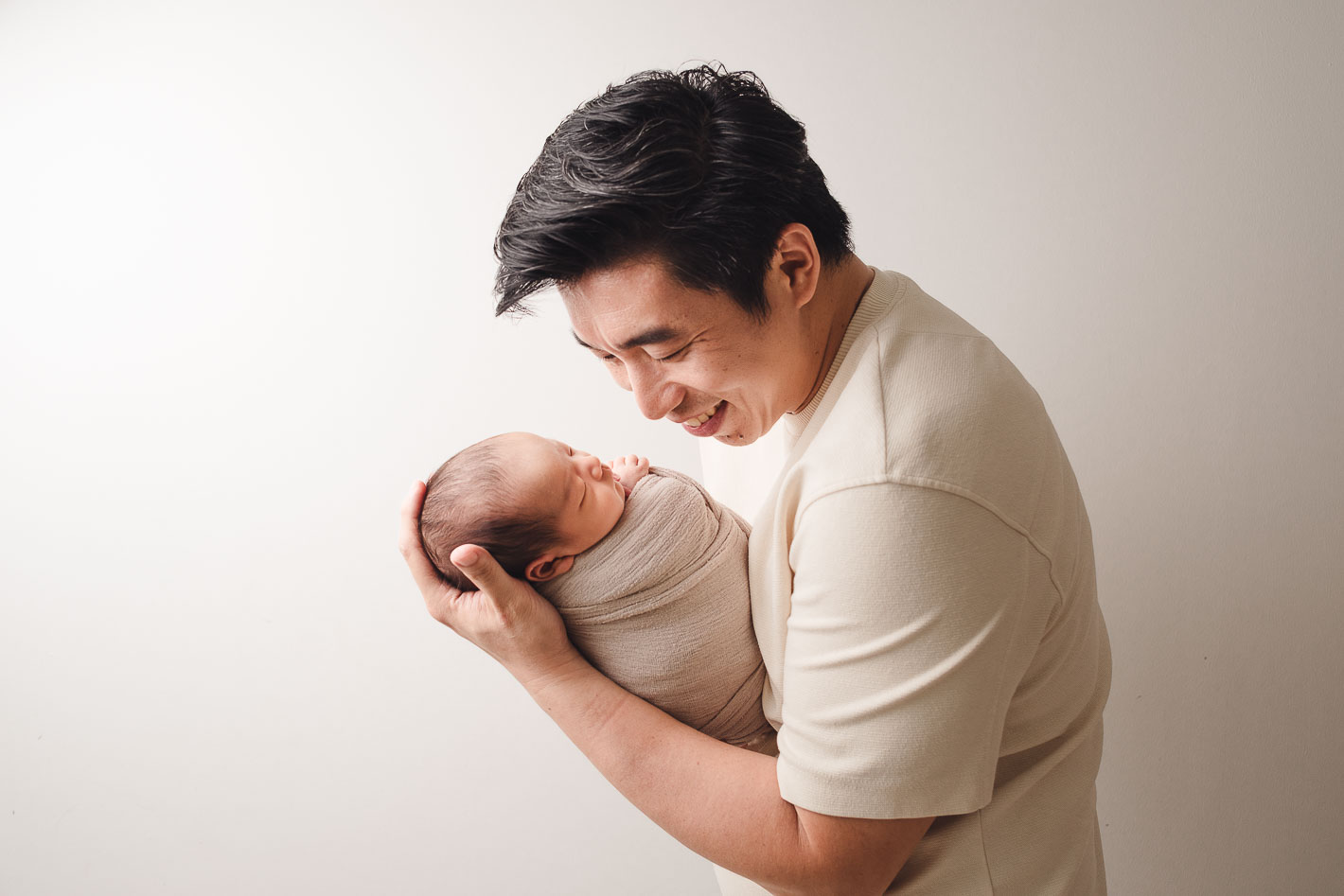 Father looking fondly at his sleeping newborn baby boy during a studio photoshoot.