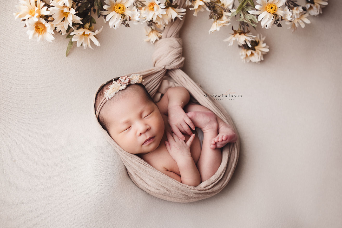 Newborn photoshoot baby suspended pose with daisies flowers.