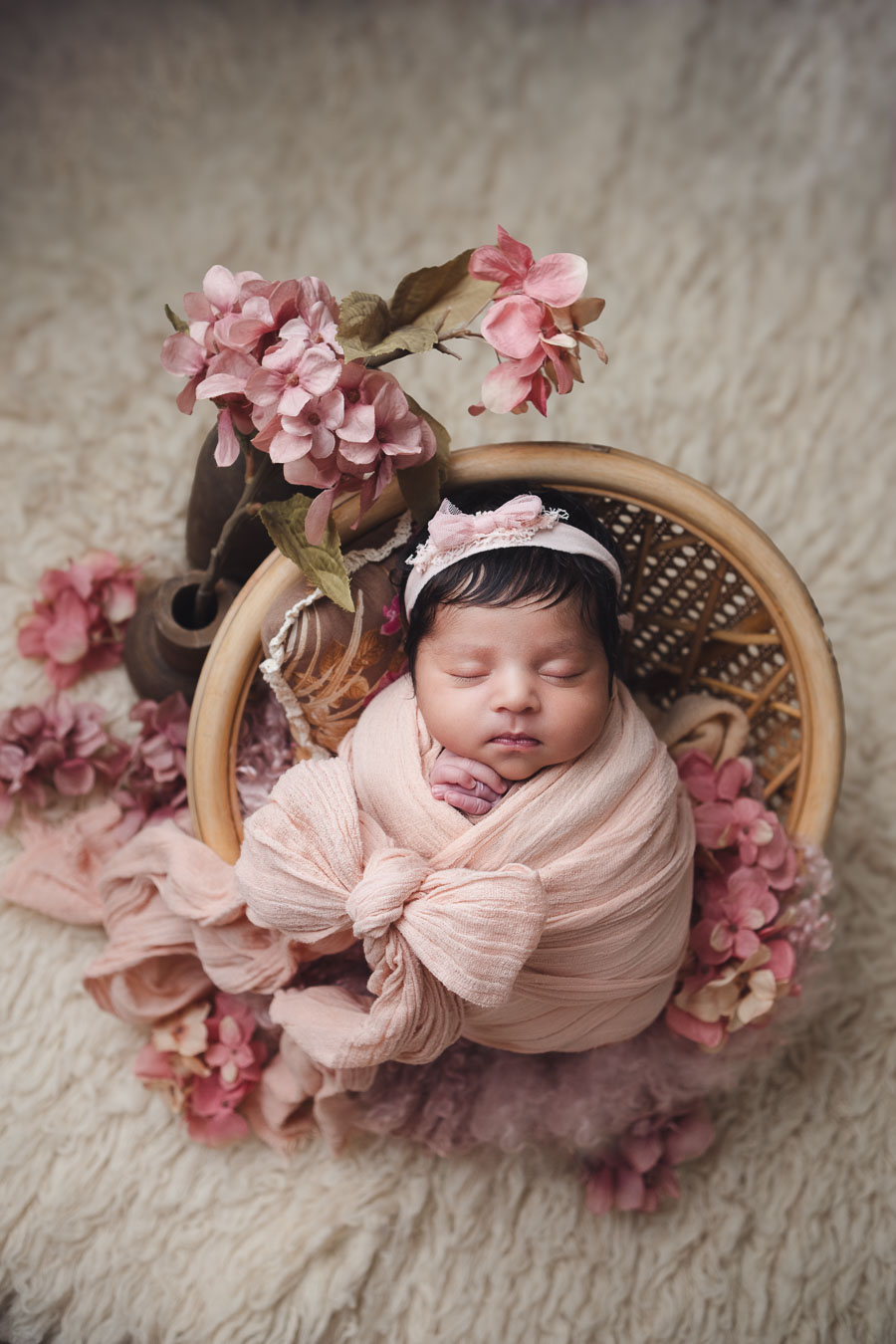 Newborn photoshoot baby wrapped in a pink with flowy ribbon and floral setup.