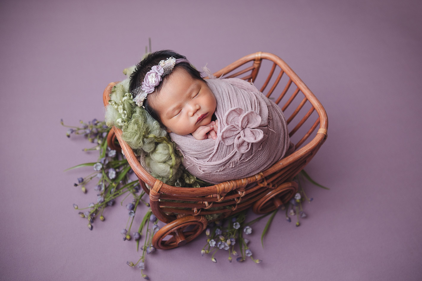 Newborn photography baby in lavender wrap sleeping in cartwheel prop