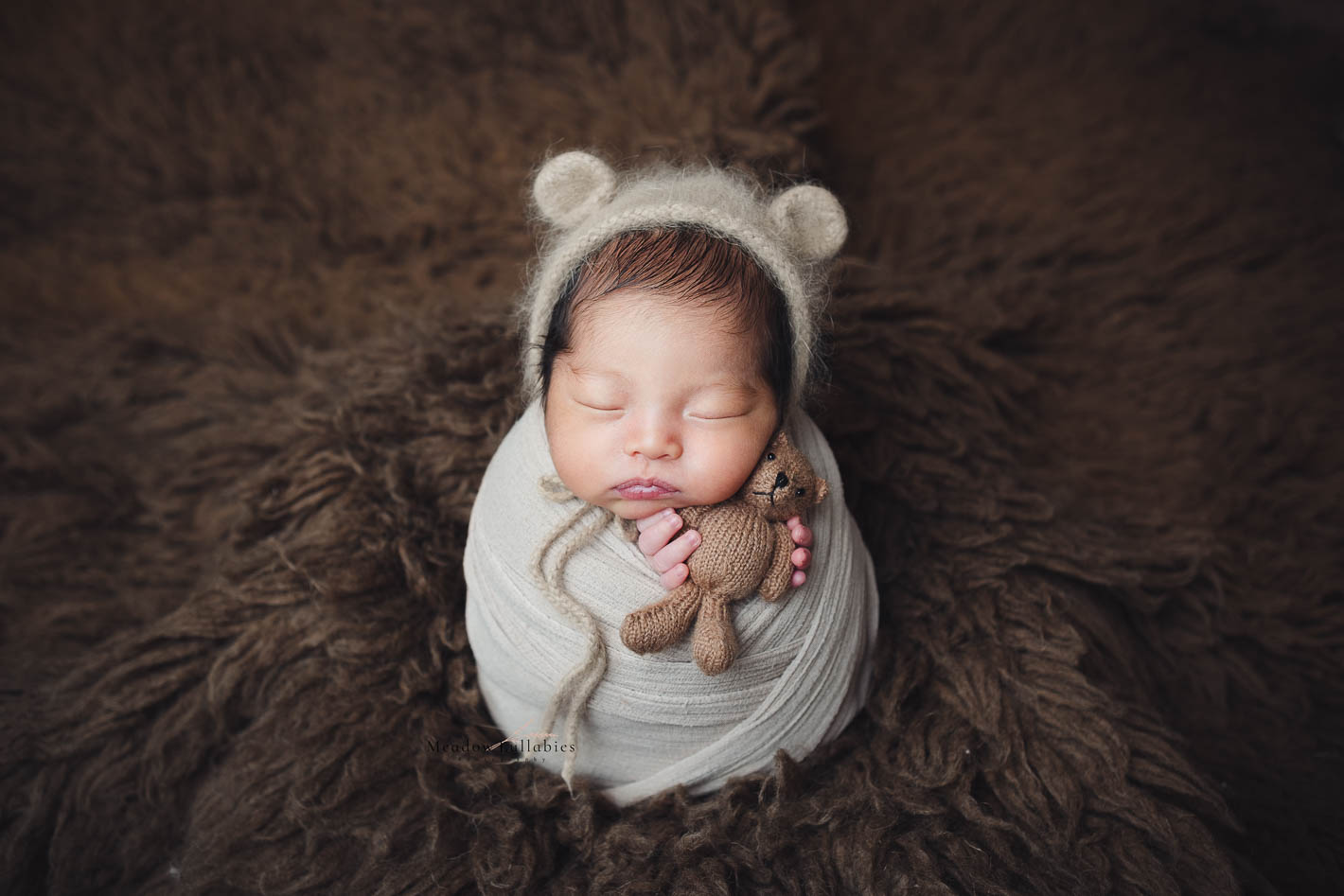 Newborn baby bundle up holding a bear soft toy