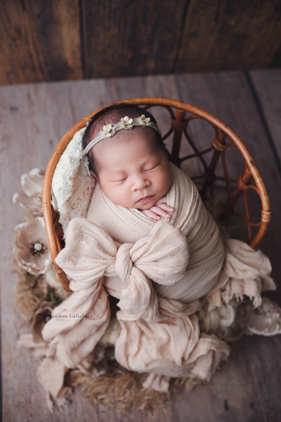 Newborn baby in neutral tone beige bow ribbon wrap sleeping on rattan chair prop