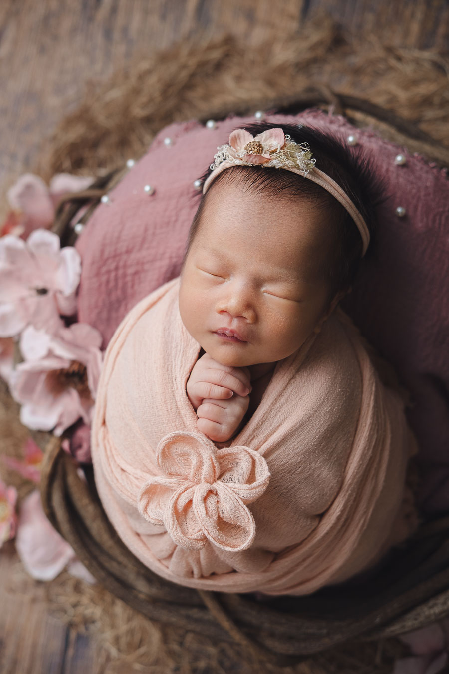Newborn baby in floral bow wrap sleeping in vintage dough bowl prop