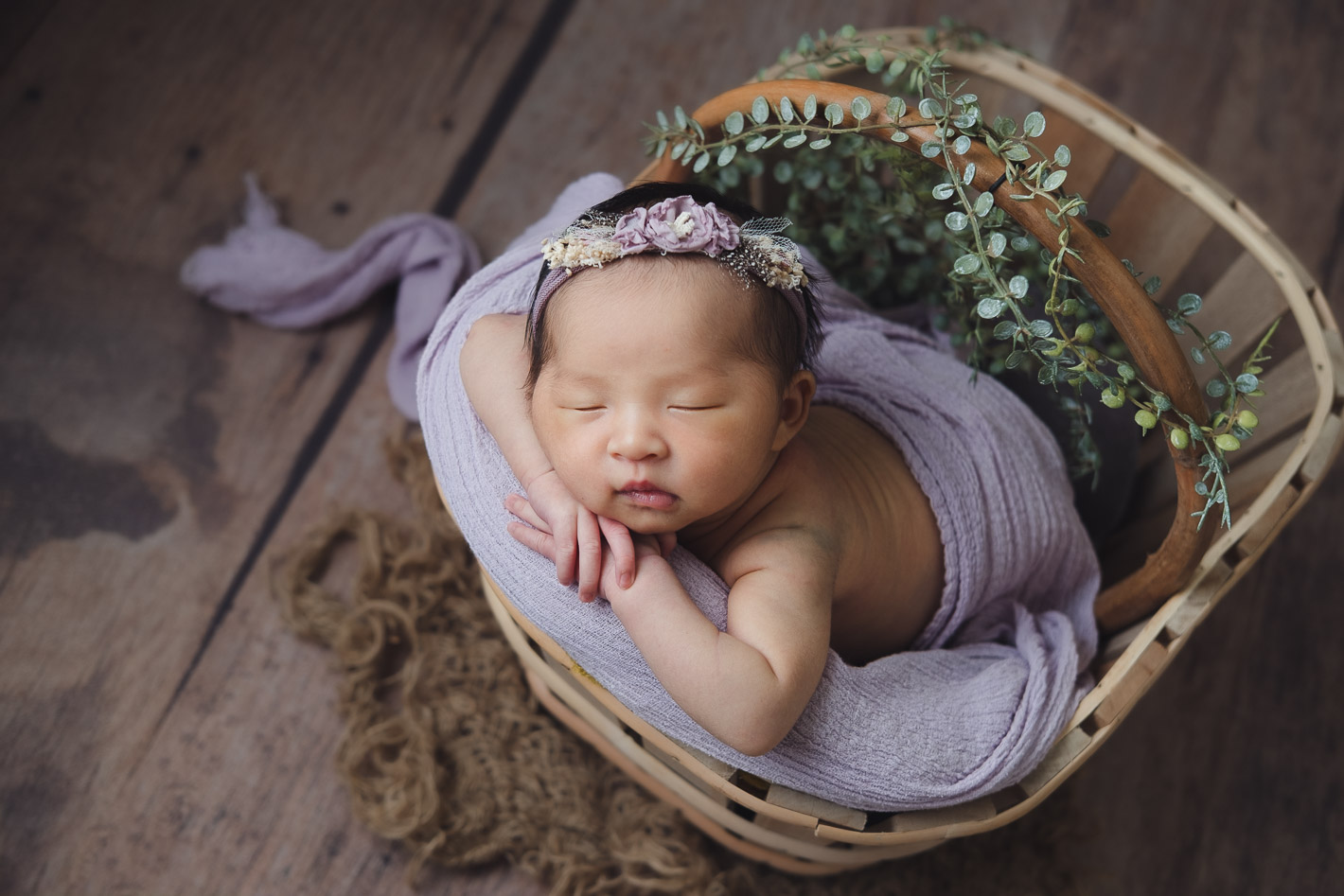 Newborn photoshoot baby posing hand under chin in crate prop on lavender drape